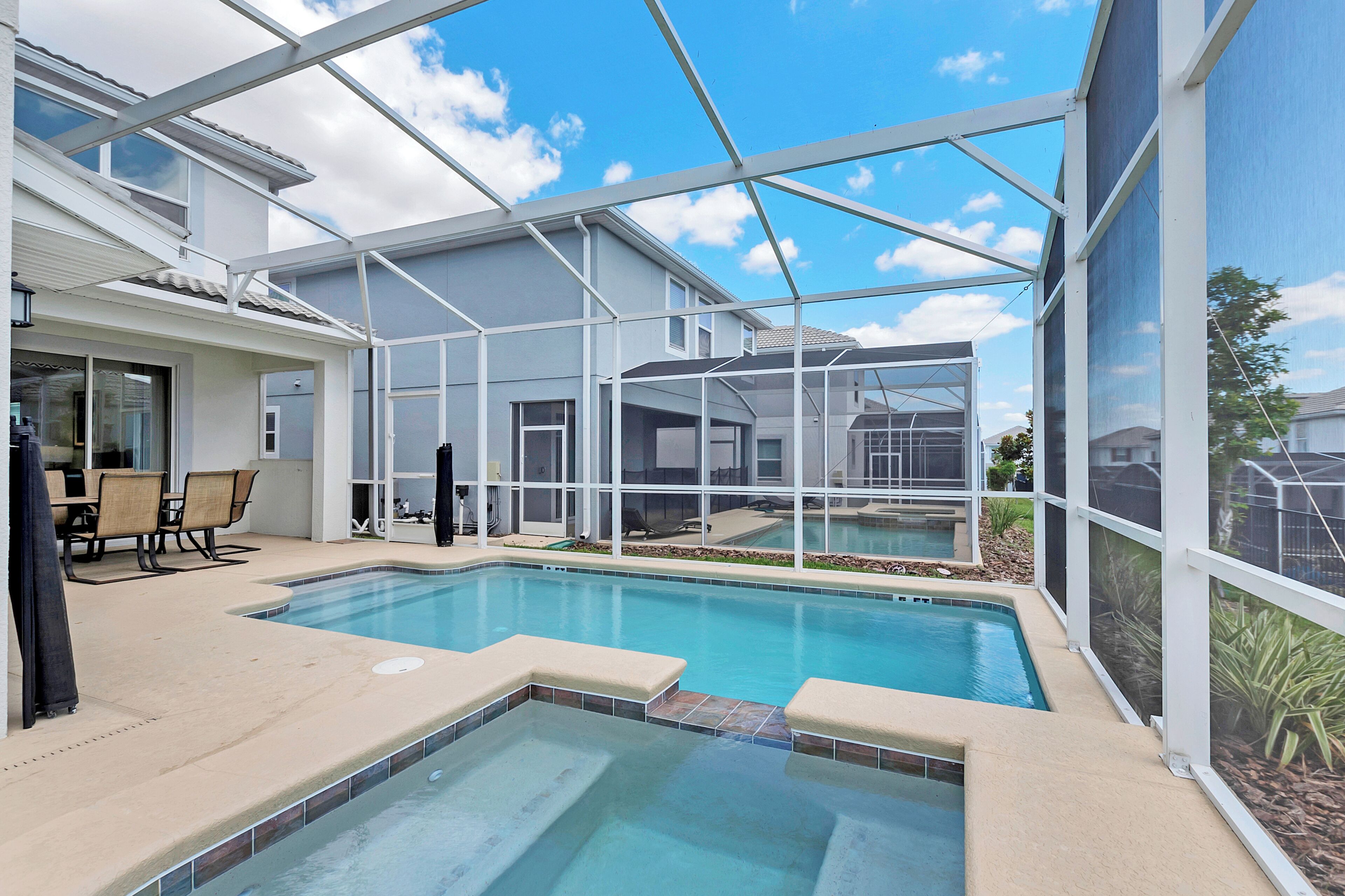 An indoor swimming pool with a glass ceiling, surrounded by a patio area with chairs and a table.