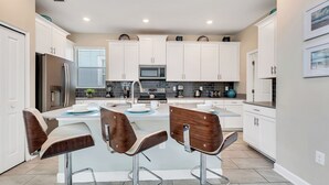 A modern kitchen with white cabinets, stainless steel appliances, and a central island with bar stools.