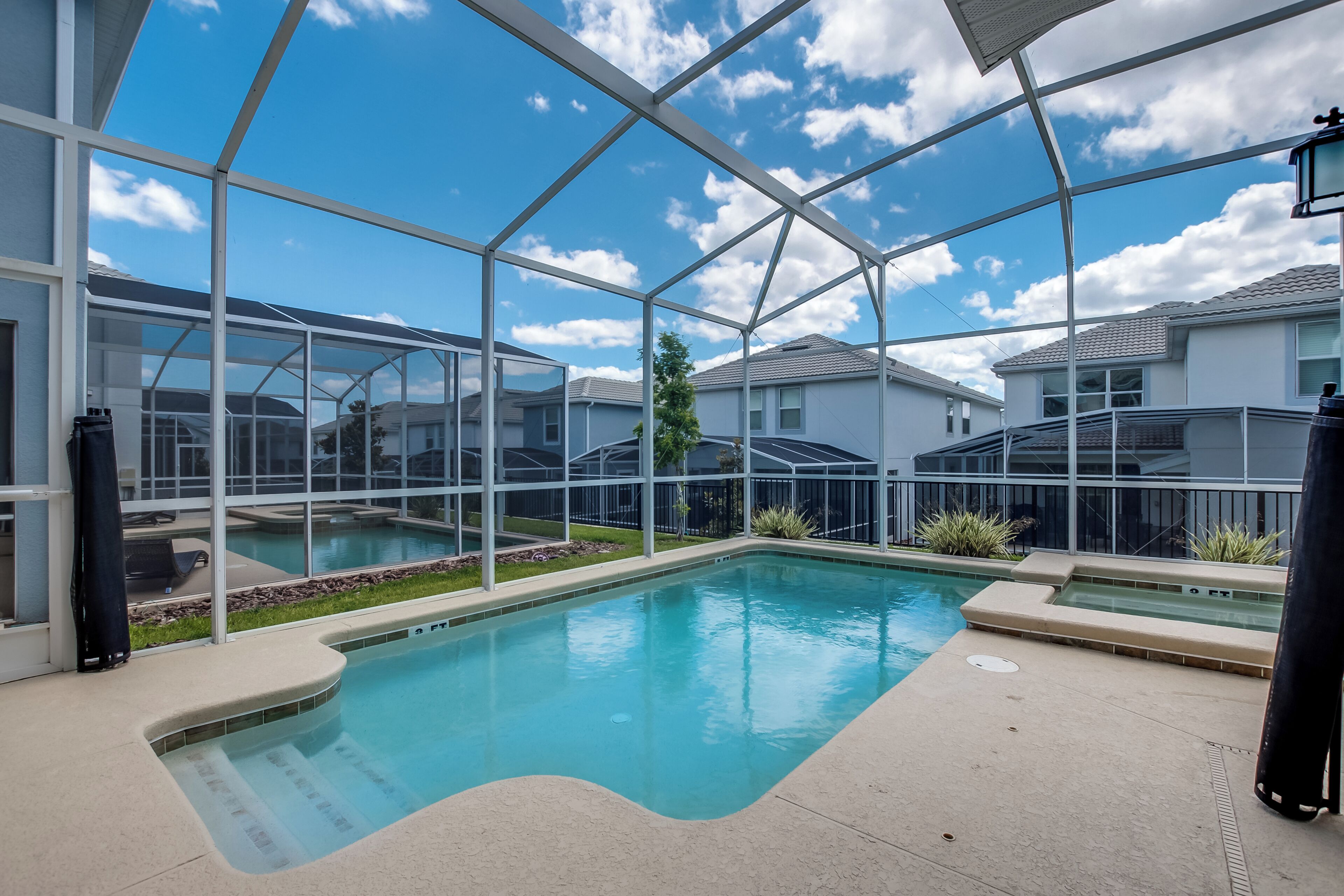 A swimming pool with a glass enclosure, surrounded by a patio area and a view of neighboring houses.