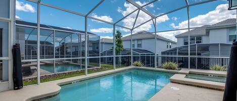 A swimming pool with a glass enclosure, surrounded by a patio area and a view of neighboring houses.