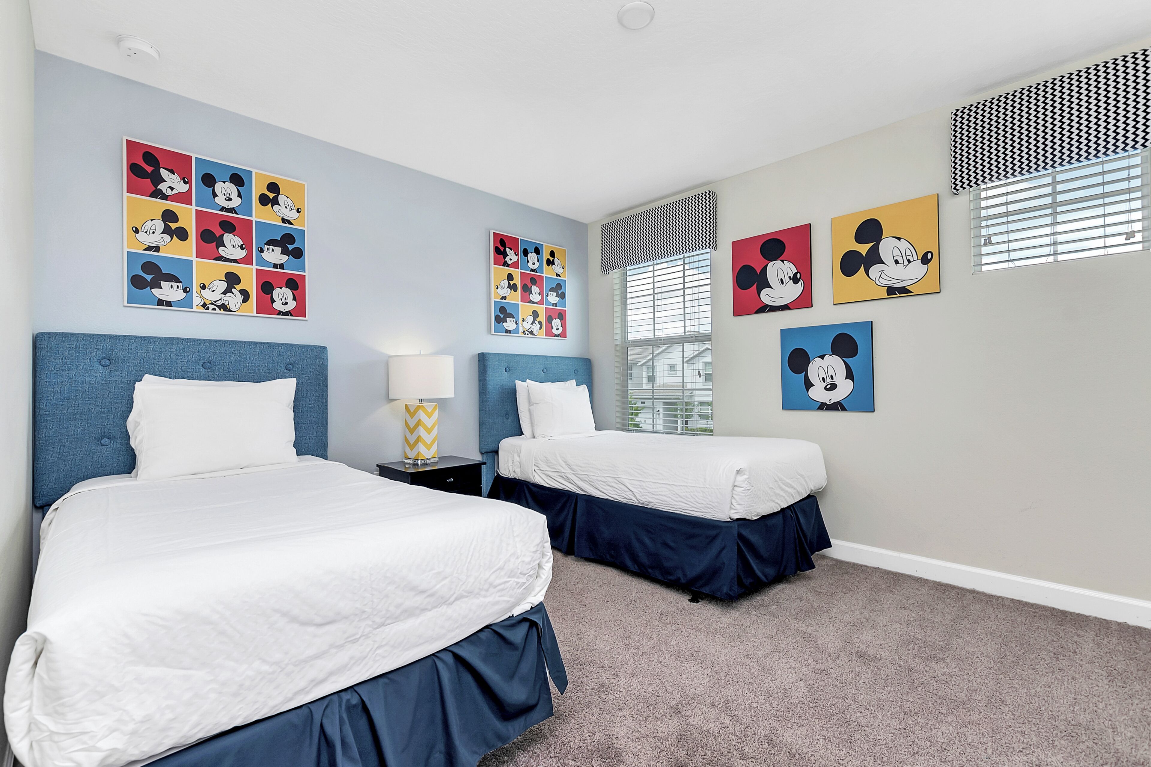 A hotel room with two beds, a window with blinds, and multiple Mickey Mouse themed wall art.