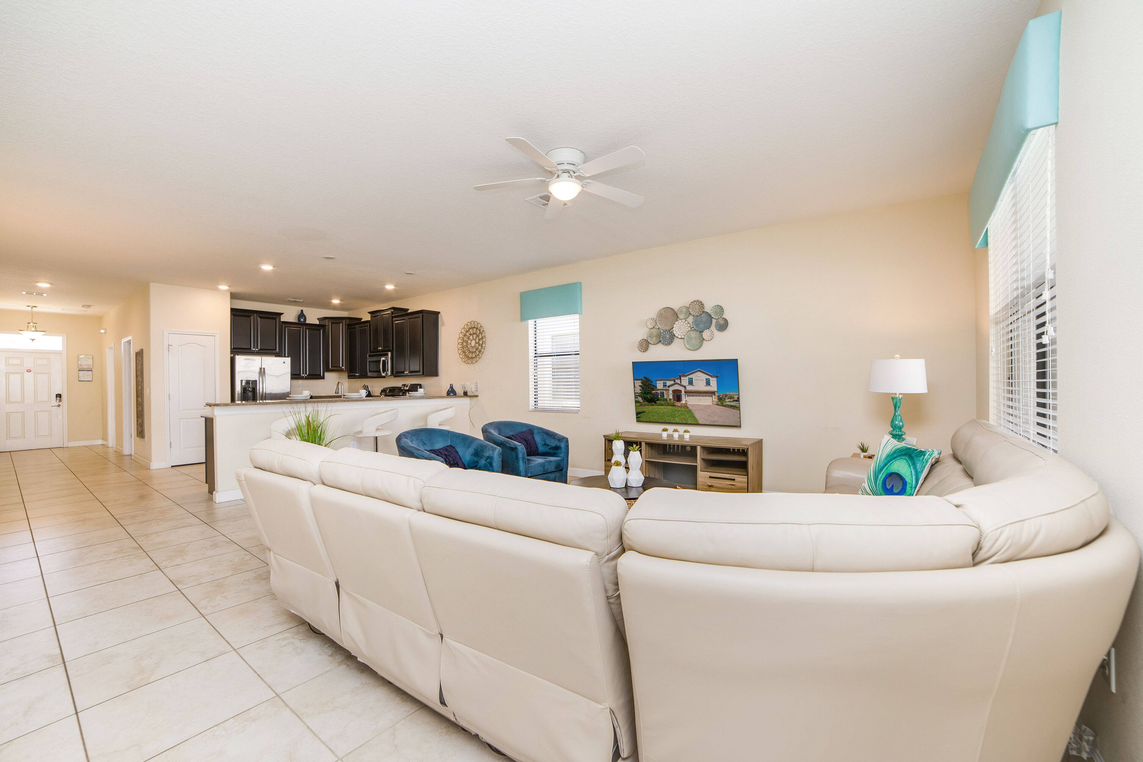 A spacious living room with a large beige sectional sofa, a ceiling fan, and a kitchen area in the background.