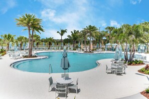A pool area with lounge chairs and umbrellas, surrounded by palm trees.