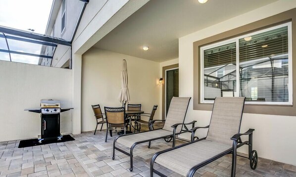 An outdoor patio with a grill, dining table, chairs, and a sun lounger. - Beautiful Townhome W/pool &free Resort Access! (Kissimmee)