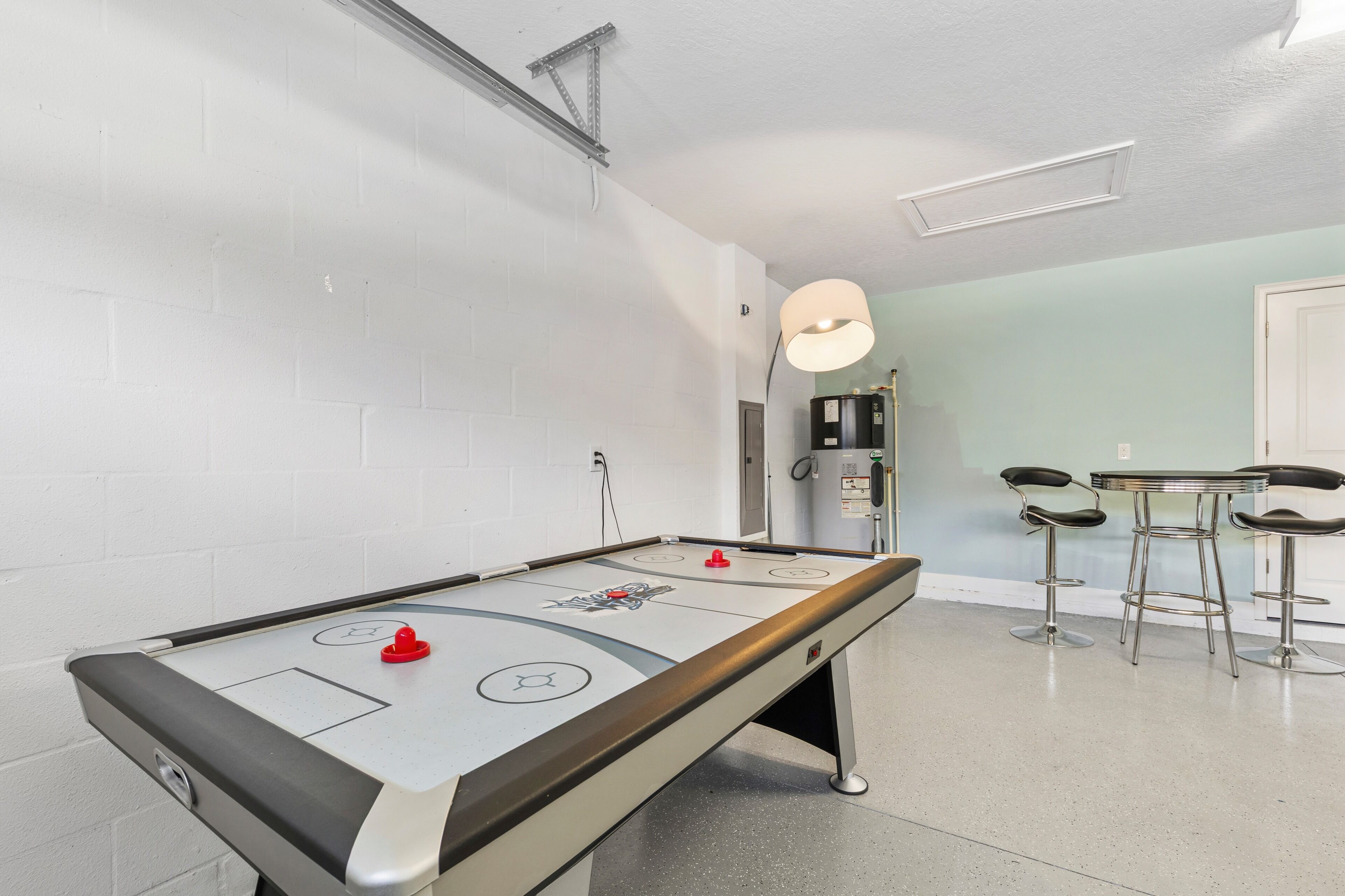 A pool table with a red puck, a bar area with stools, and a water dispenser in a room with white brick walls and a light green accent wall.