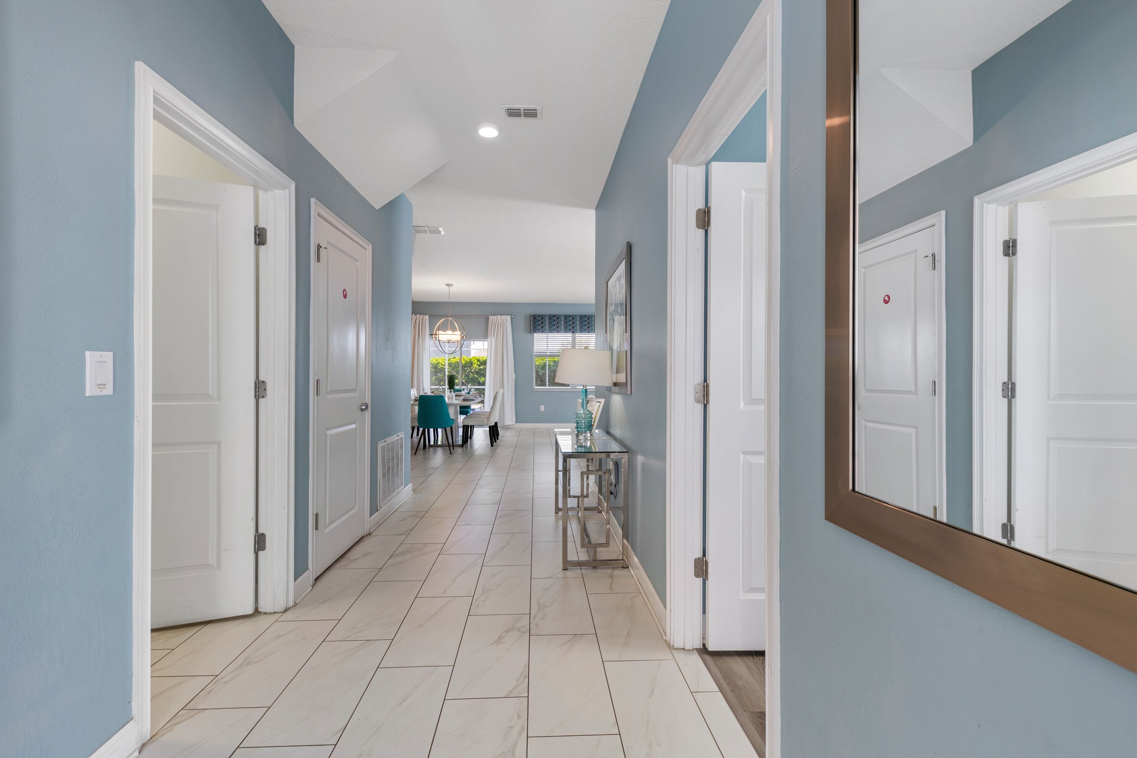A hallway with white doors, light blue walls, and a tiled floor.