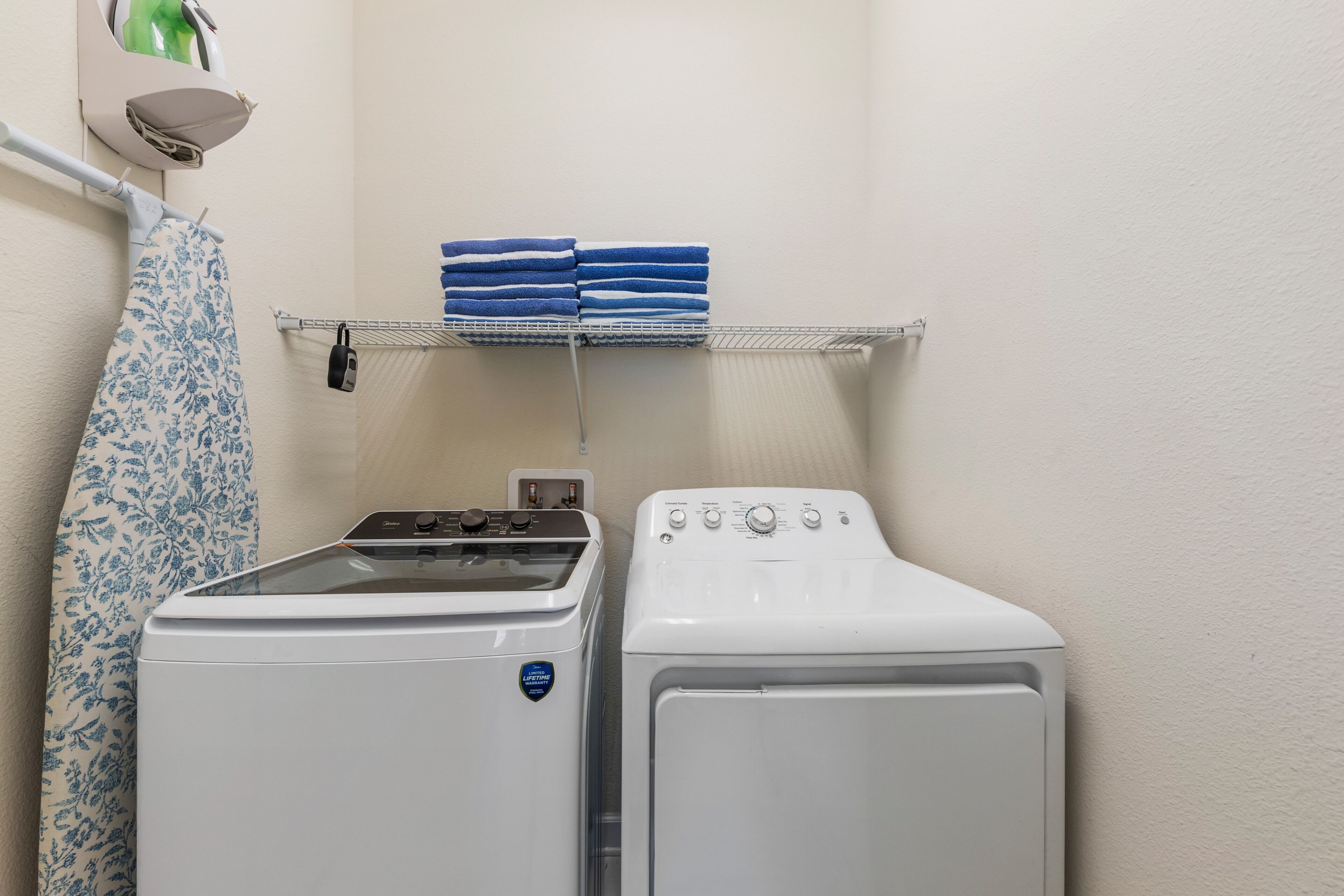 Un espace buanderie comprenant un lave-linge et un sèche-linge, un porte-serviettes avec des serviettes pliées, et une serviette à motifs suspendue à un étendoir.