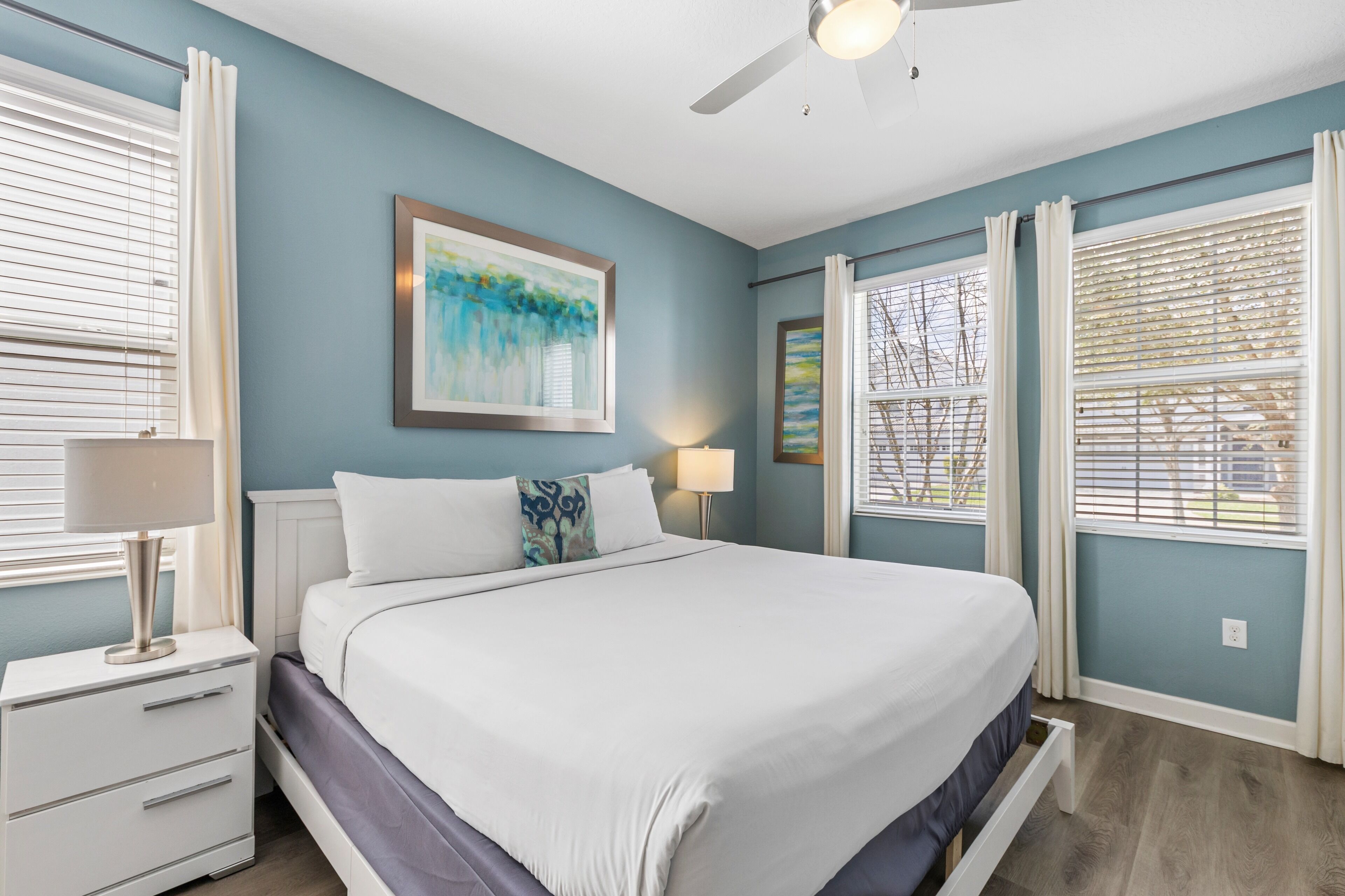 A bedroom with a bed, nightstands, a ceiling fan, and a window with blinds.