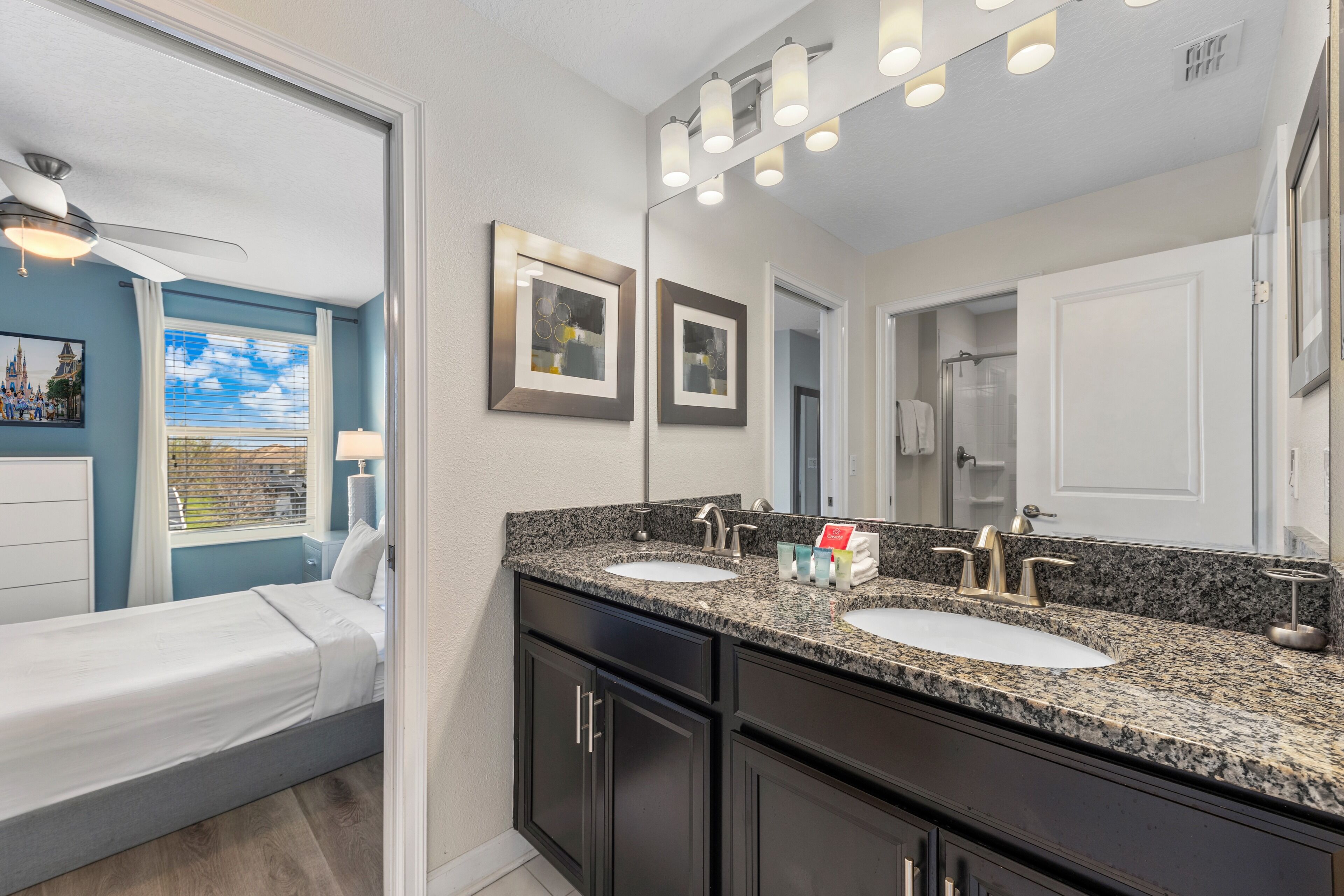 A modern bathroom with two sinks, dark cabinetry, a large mirror, and a ceiling fan.