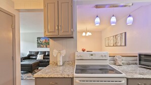A kitchen with a stove, oven, and microwave. There is a dining area with a couch and a painting on the wall. - Gold Creek Condo: Downtown, Amazing Views (Breckenridge)