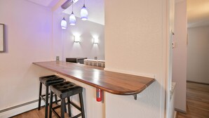 A kitchen with a wooden countertop, two black bar stools, pendant lighting, and a white wall. - Gold Creek Condo: Downtown, Amazing Views (Breckenridge)