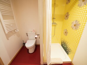 Un baño con un inodoro blanco, una ducha con pared de diseño amarillo y un suelo rojo.
