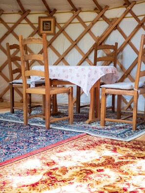 Una habitación con una mesa y sillas de madera, un tapete estampado y una estructura tipo tienda de campaña al fondo.
