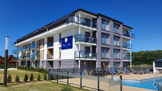 Un hotel de varios pisos con piscina, asientos al aire libre y un cartel que dice "BALTIN".
