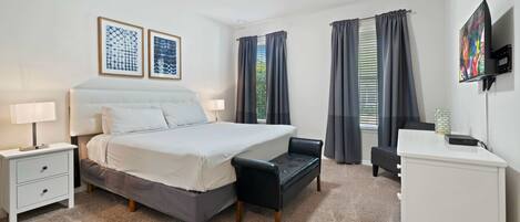 A bedroom with a bed, bedside tables, a desk, a chair, and a TV.