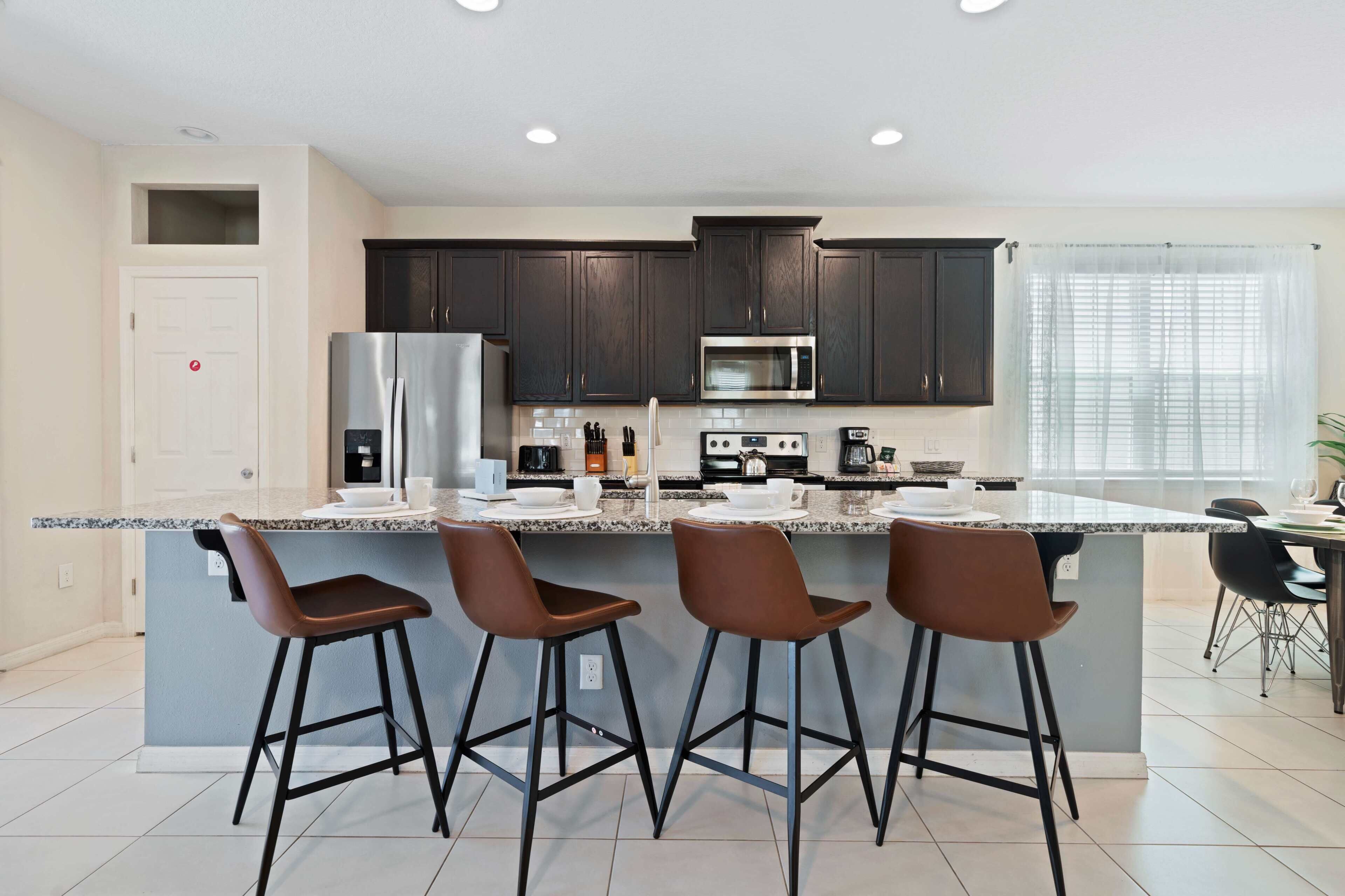A modern kitchen with dark cabinets, a central island with bar stools, and a dining area with a table and chairs.