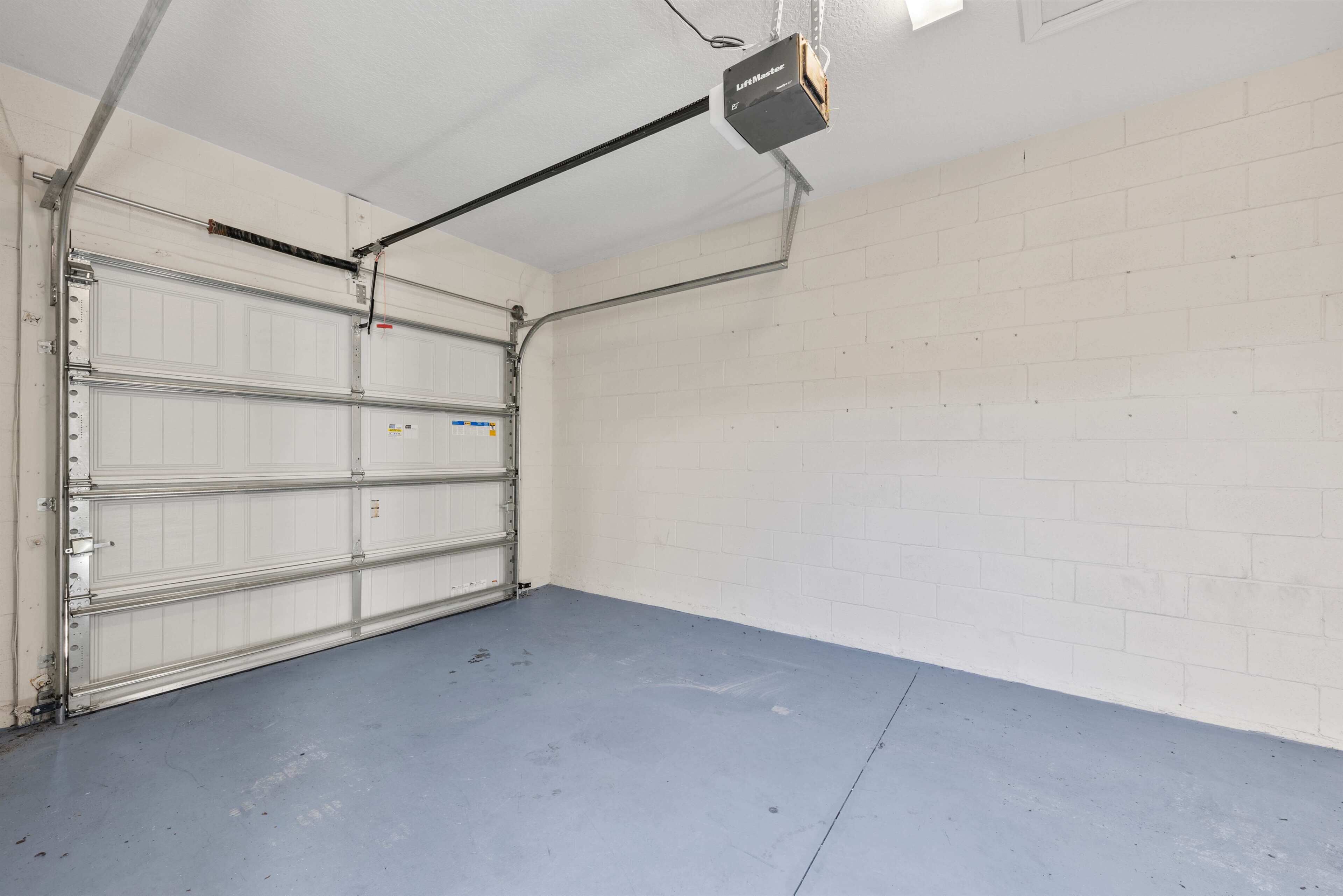 A garage with a closed metal garage door, a blue floor, and a white brick wall.