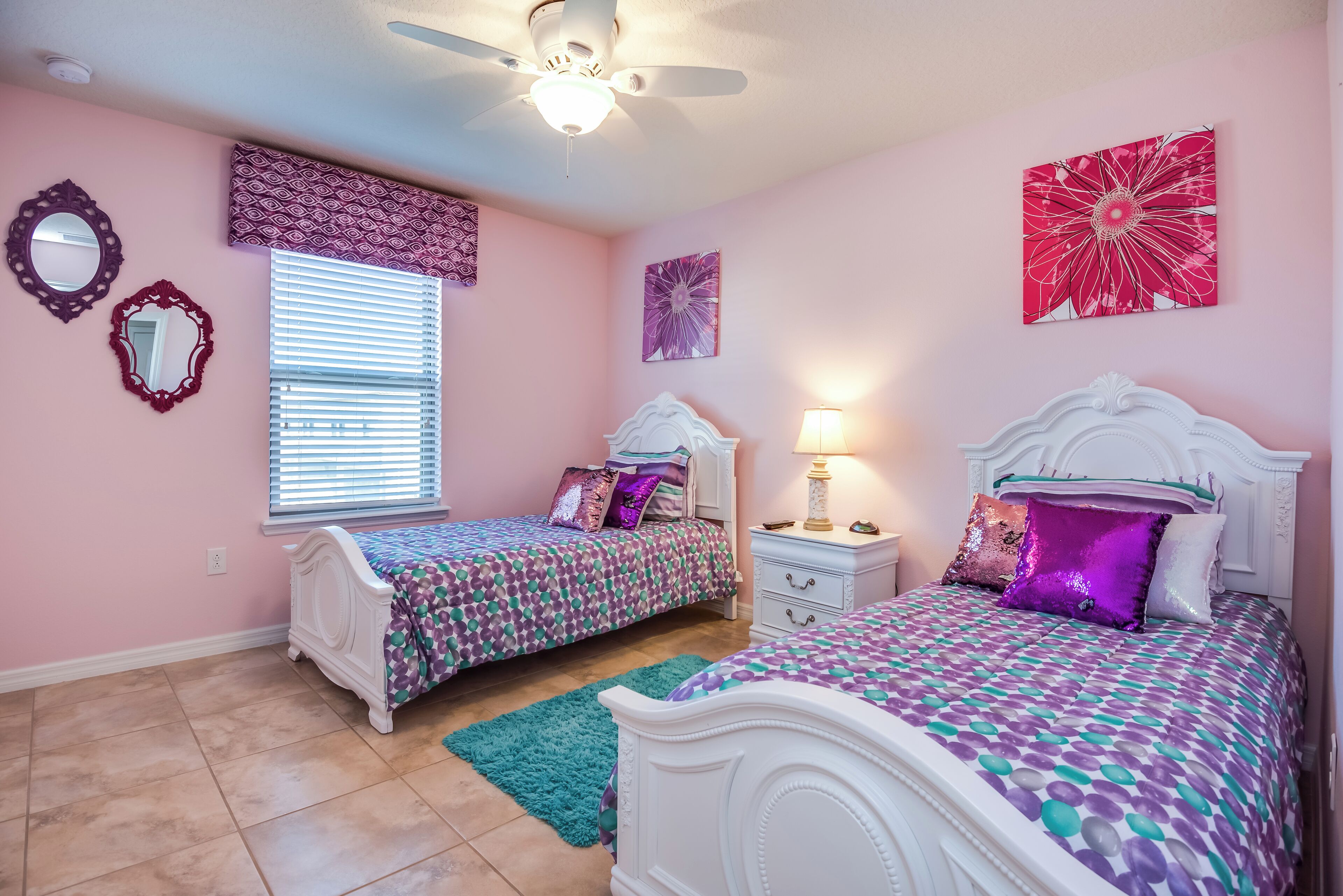A bedroom with two beds, a ceiling fan, and a window with blinds.