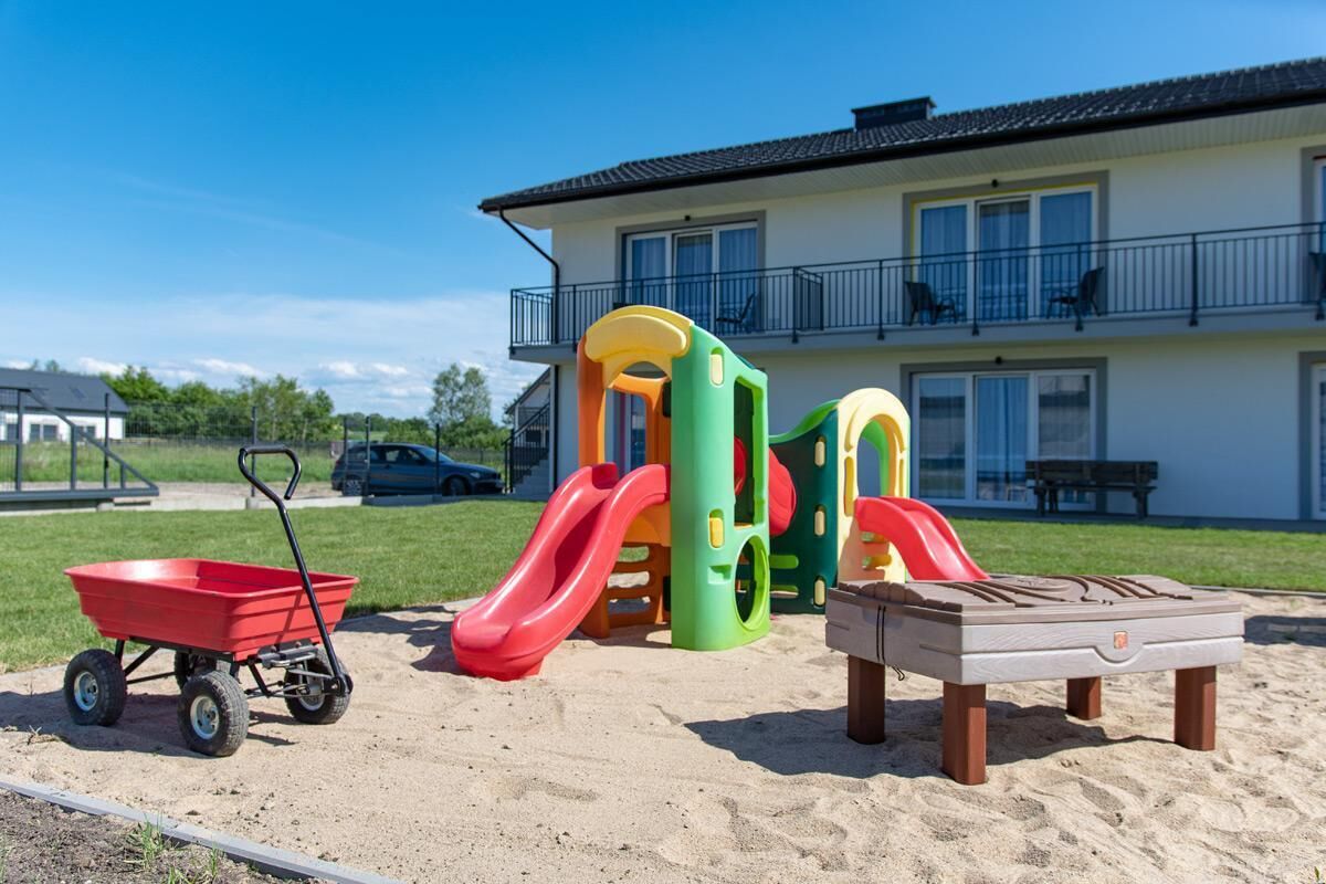 A playground with slides and a sand table in front of a building with a balcony.