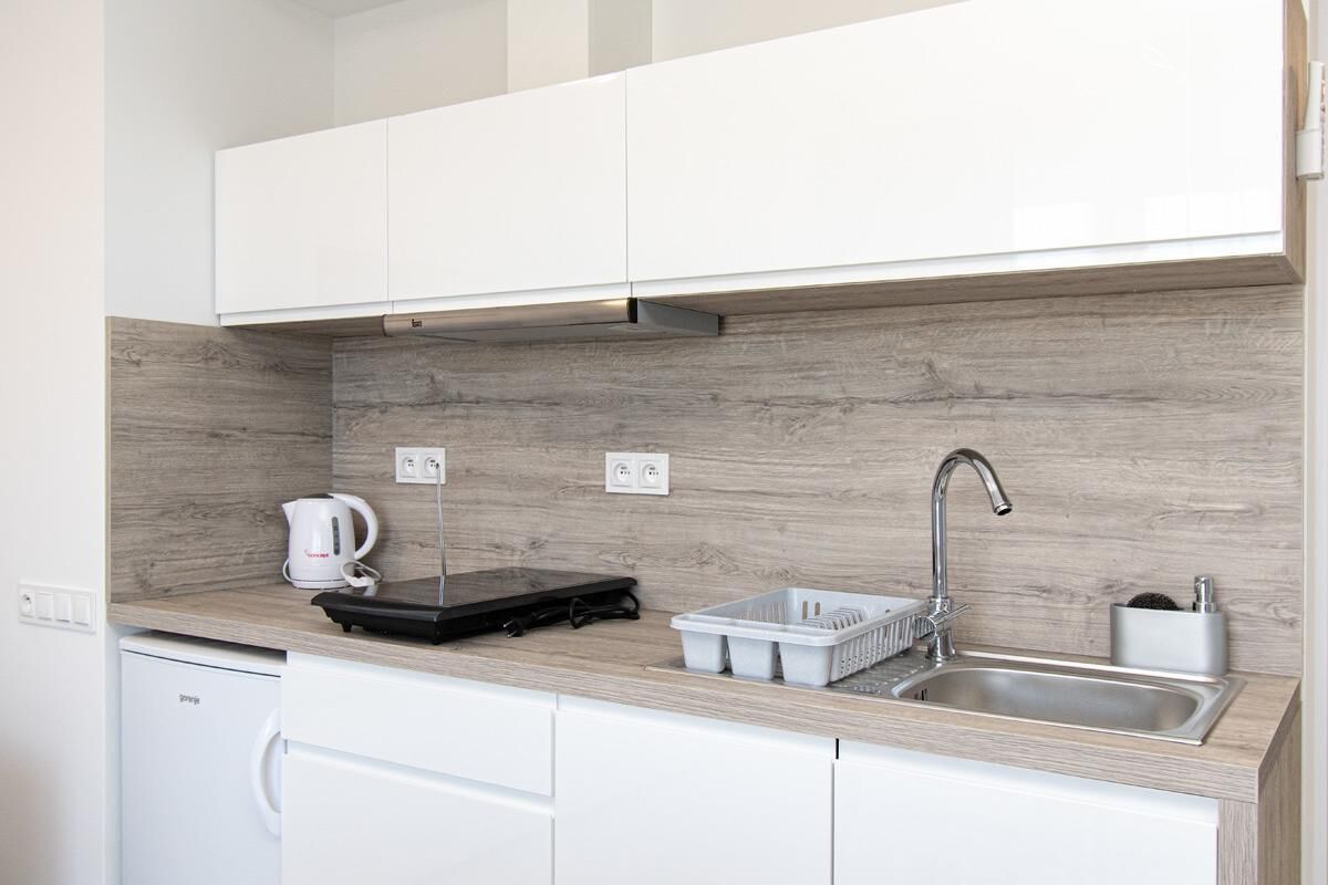 A compact kitchen with white cabinets, a wooden backsplash, a built-in sink, and a compact refrigerator.