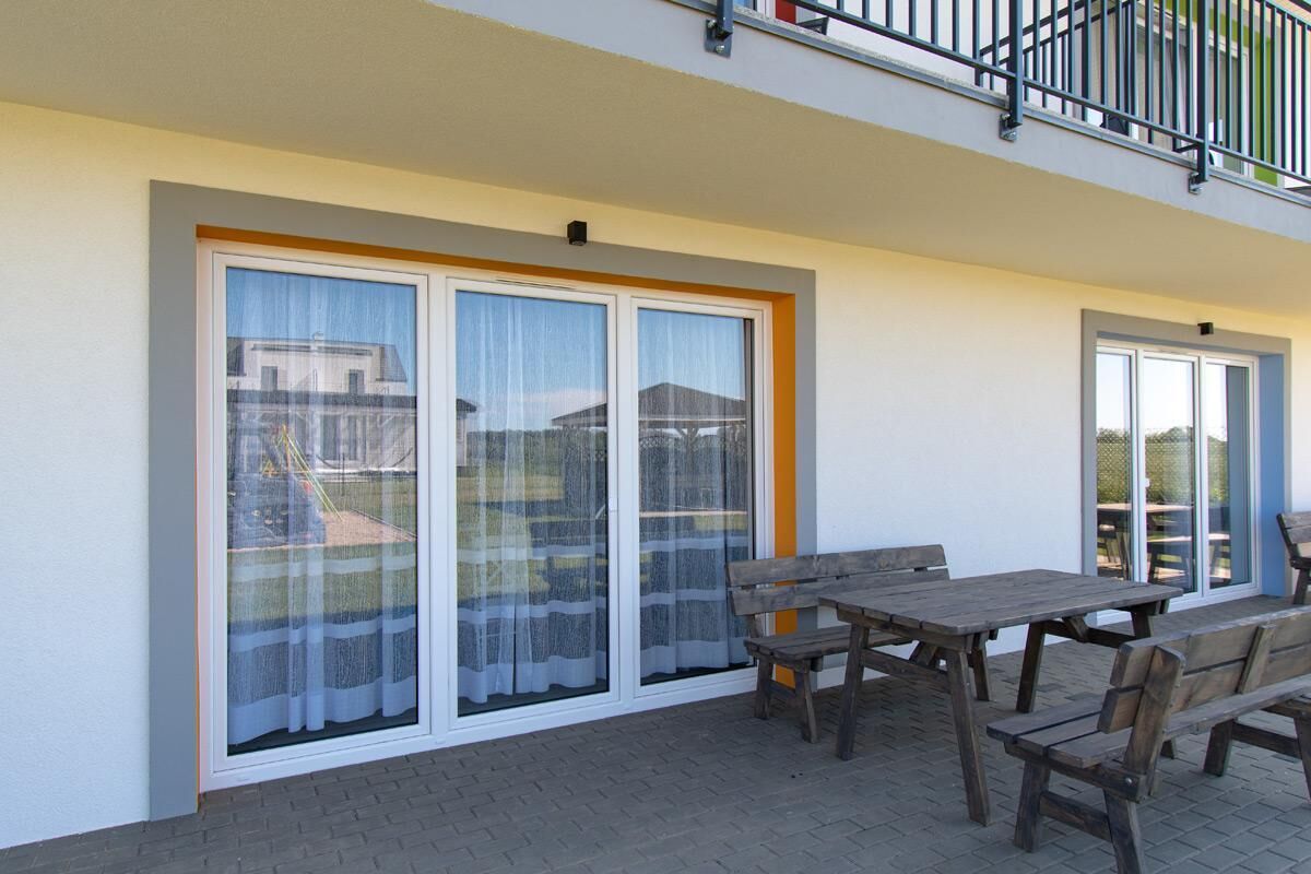 A balcony with a wooden table and chairs, large sliding glass doors, and a metal railing.