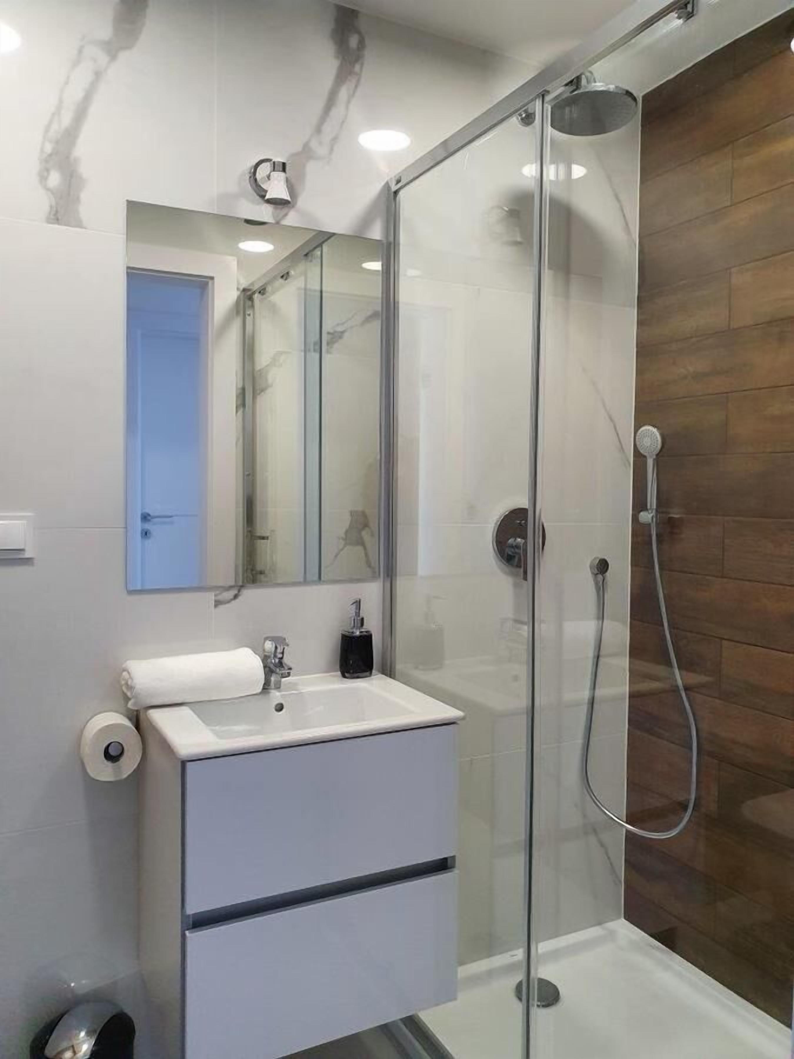 Ein modernes Badezimmer mit einer gläsernen Duschkabine, einem weißen Waschbecken mit Spiegel darüber und einer Holzwand.