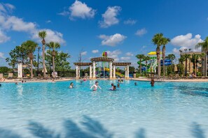 Ein Schwimmbad mit Schwimmern und spielenden Personen, umgeben von Palmen und einem Wasserpark.