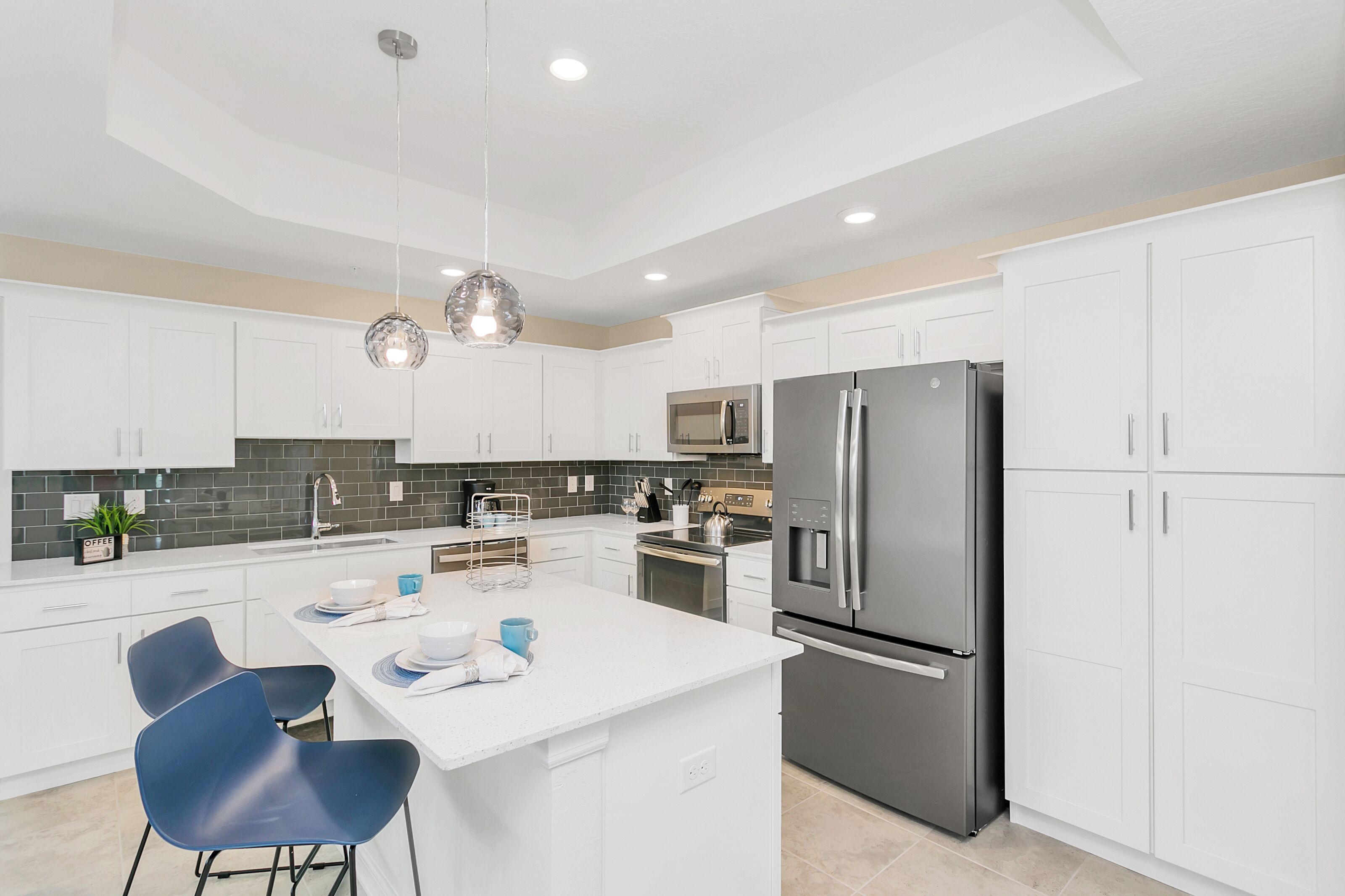 A modern kitchen with white cabinetry, a stainless steel refrigerator, a microwave, and a central island with seating.