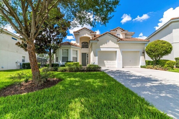 A residential house with a well-maintained lawn, a garage, and a large tree in the front yard.