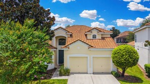 A two-story house with a red-tiled roof, a front garage, and a well-maintained lawn. - Spacious Home W/private Pool/spa & Free Waterpark! (Kissimmee)