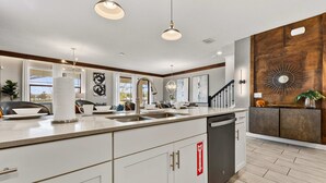A modern kitchen with white cabinetry, a large island, stainless steel appliances, and a wooden accent wall. - 2911 Fable Street (Kissimmee)