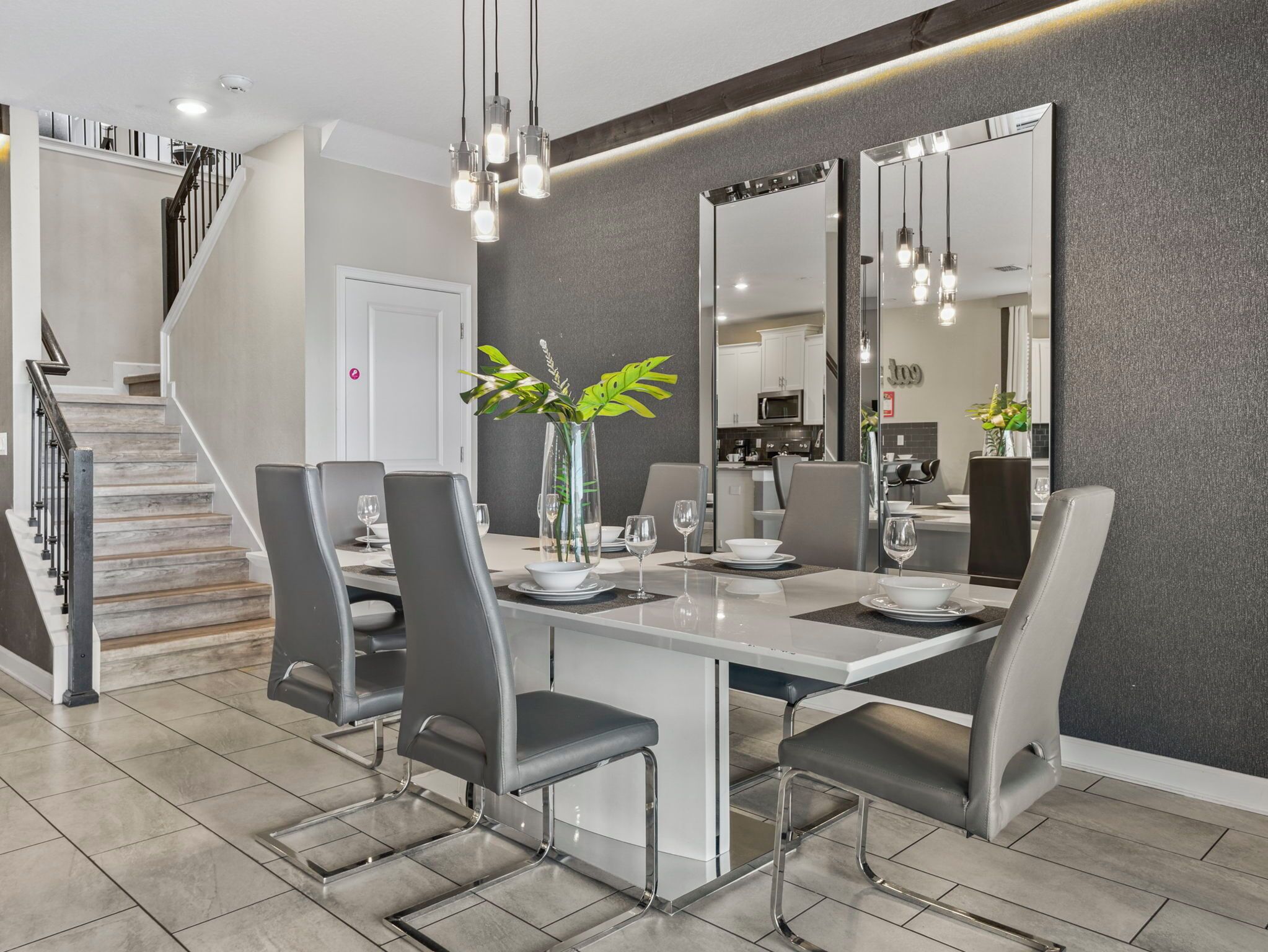 Un espace repas moderne avec un îlot central, des chaises grises et un vase orné de plantes.