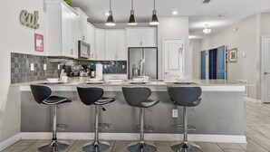 A modern kitchen with a central island, bar stools, and pendant lighting. - Private Pool/spa & Gameroom, Near Wdw! Sleeps 25 (Kissimmee)
