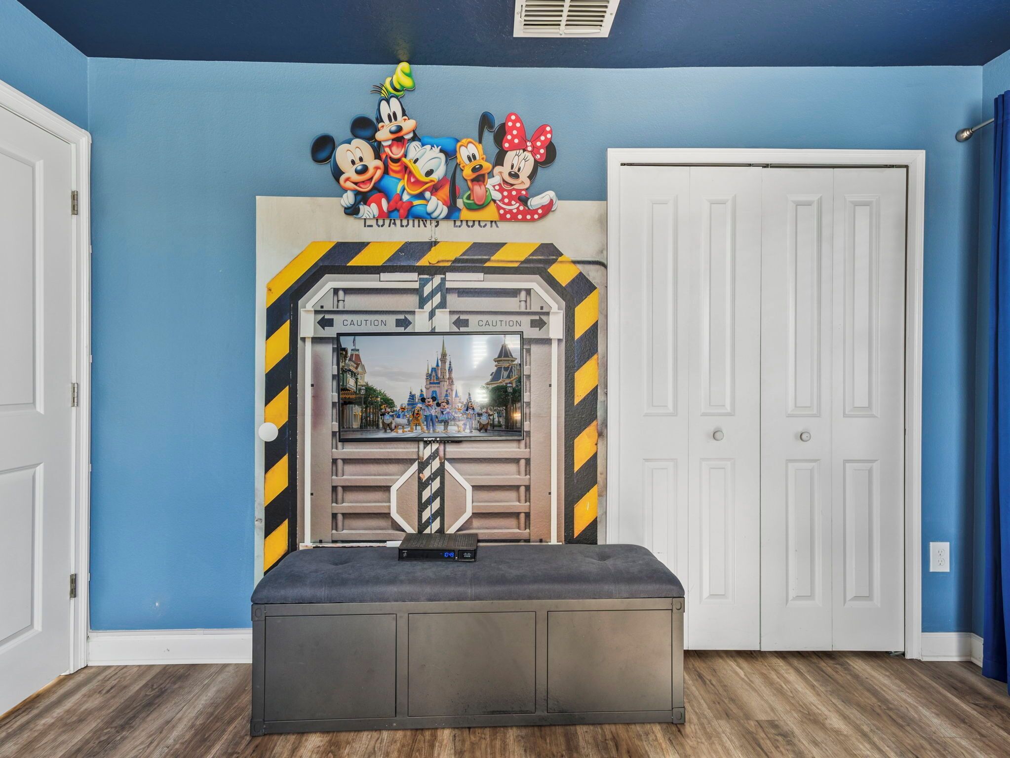 A room with blue walls, a Disney-themed mural, a large window, and a grey bench.