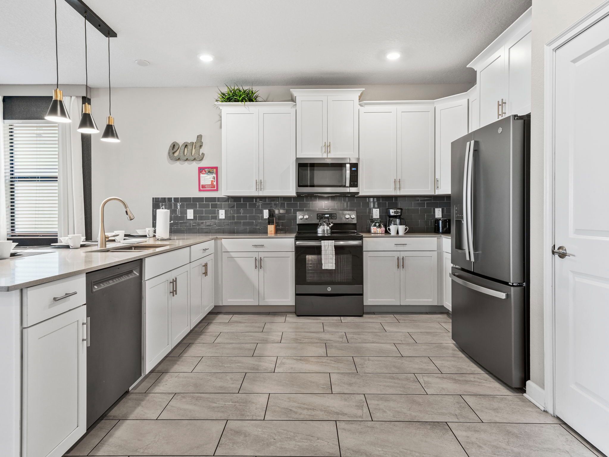 A modern kitchen with white cabinets, a stainless steel refrigerator, a microwave, and a stove.