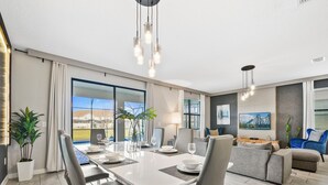 A modern living room with a dining area, large windows, and a view of the outside. - Private Pool/spa & Gameroom, Near Wdw! Sleeps 25 (Kissimmee)