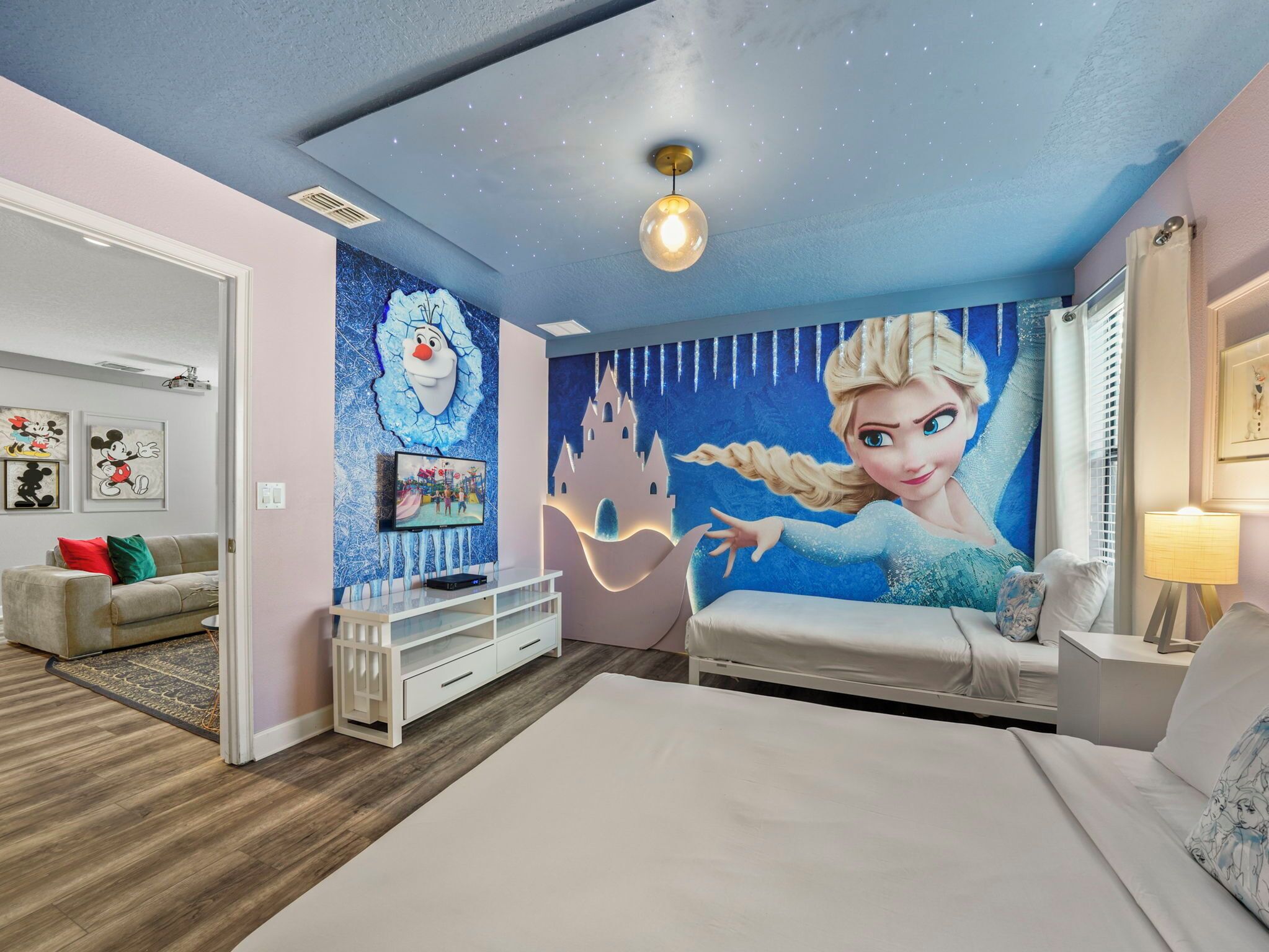 Une chambre d’enfant avec une fresque représentant un personnage, un téléviseur, une commode blanche et un lit.
