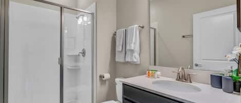 A modern bathroom with a glass shower enclosure, a white toilet, a vanity with a sink, and a large mirror.