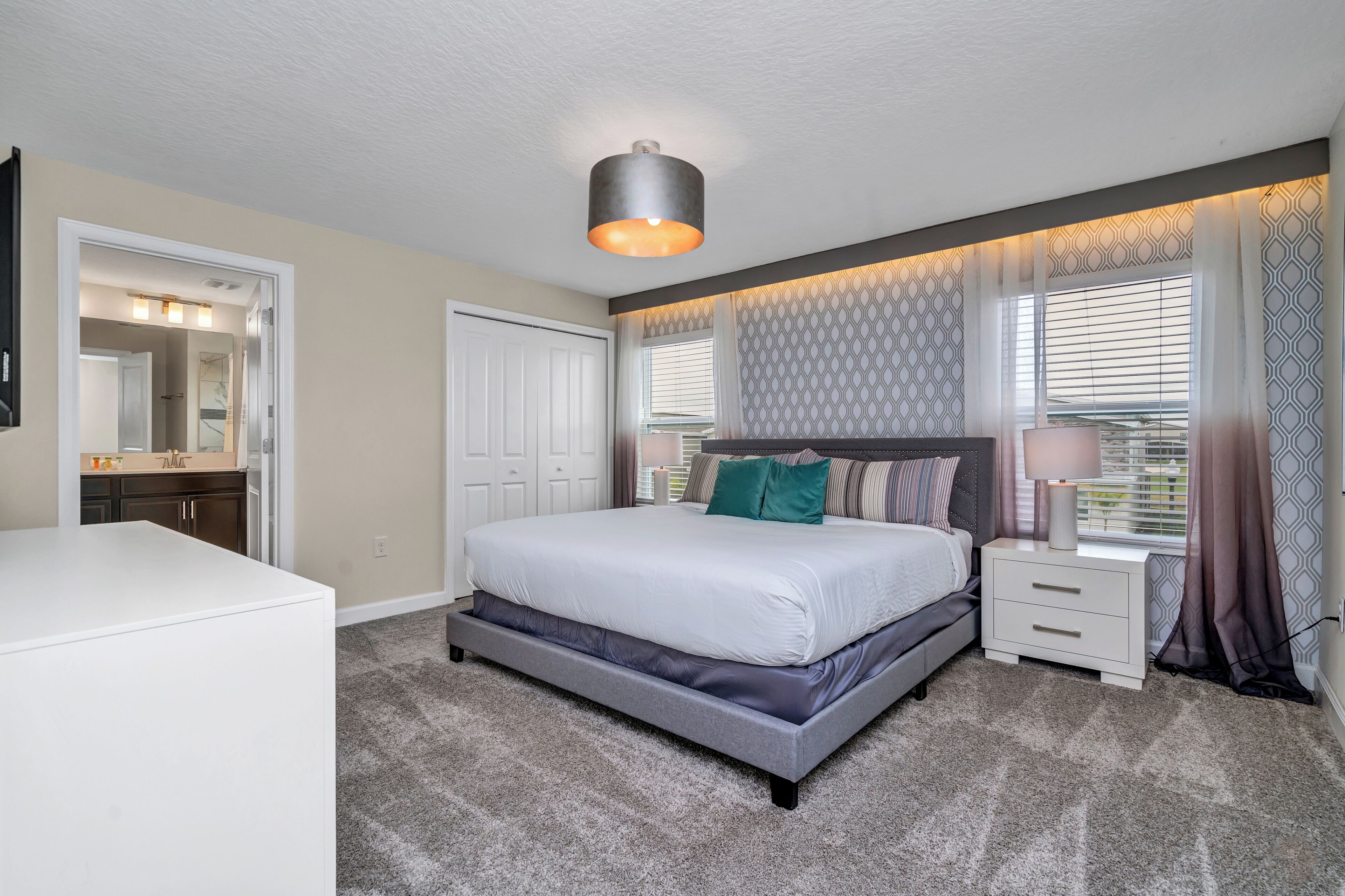 A bedroom with a bed, bedside tables, a nightstand, a mirror, and a ceiling light fixture.