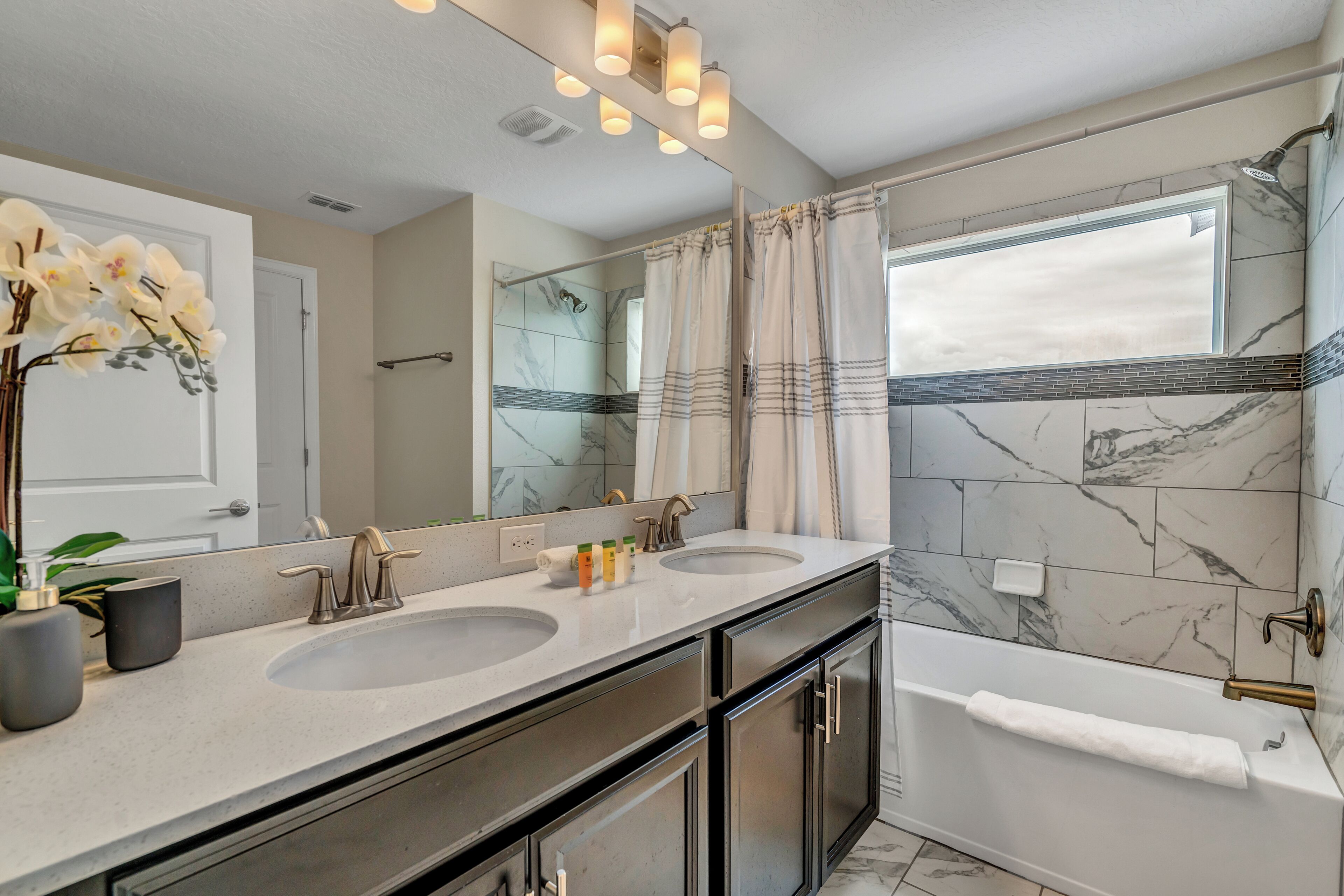 A modern bathroom with two sinks, a large mirror, a bathtub, and a shower with a glass door.