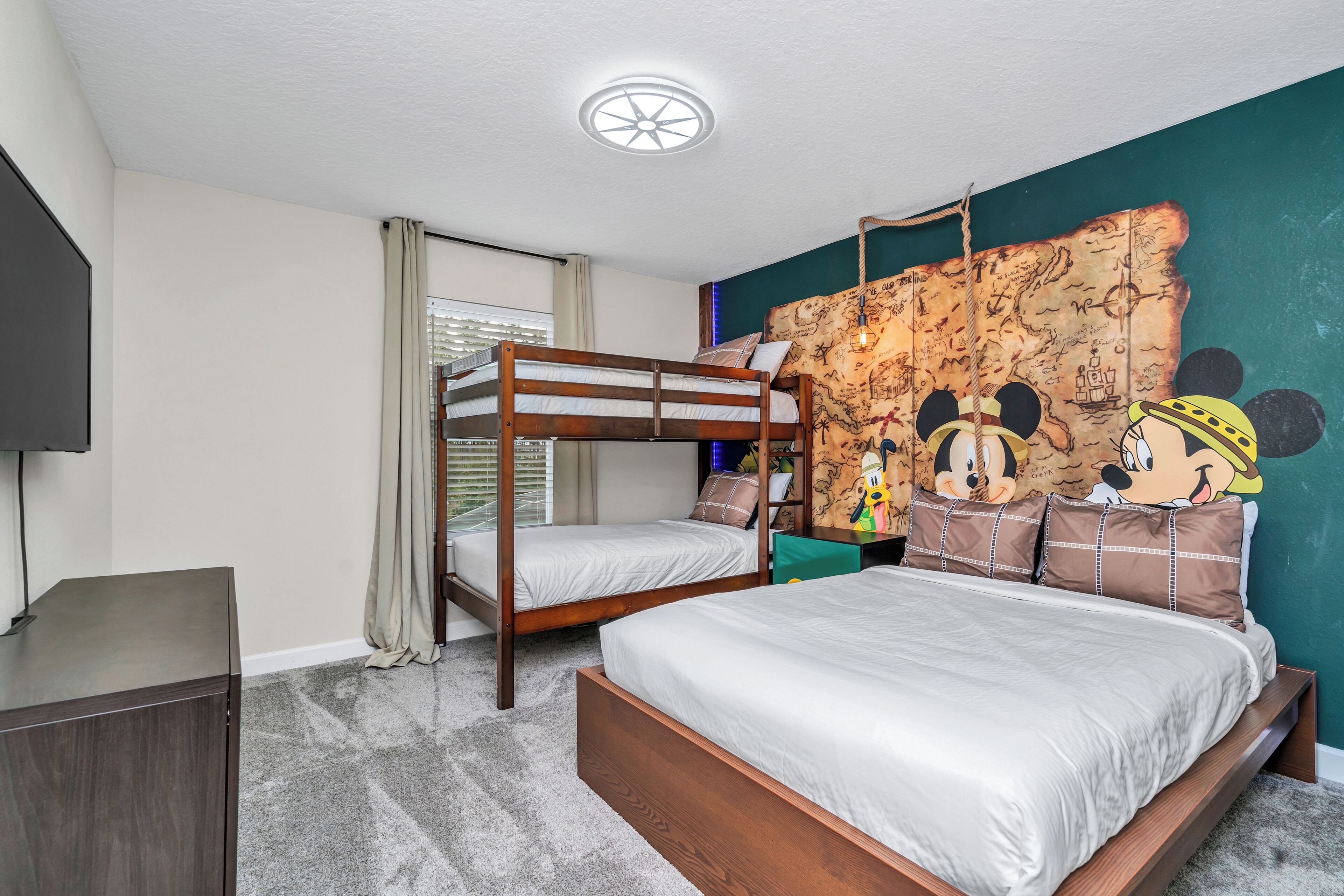 A room with bunk beds, a desk, a map mural, and a television.