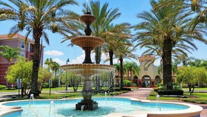 Una fuente escalonada rodeada de palmeras y un edificio con ventanales de arco.