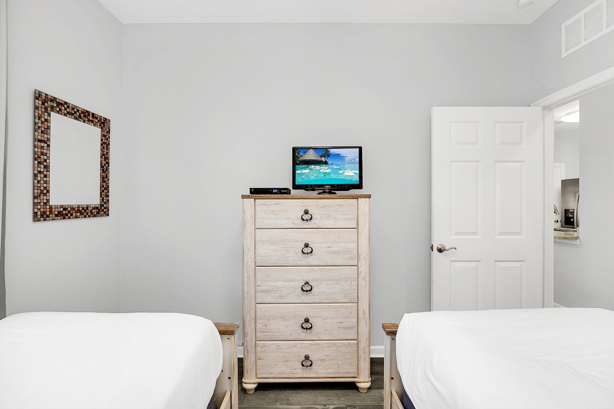 Une chambre avec deux lits, une commode sur laquelle est posée une télévision, et une porte blanche.