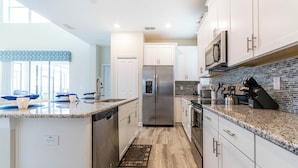 A modern kitchen with white cabinets, a stainless steel refrigerator, granite countertops, and a backsplash with a mosaic tile pattern. - Beautiful Home W/private Pool & Spa, Near Wdw! (Kissimmee)