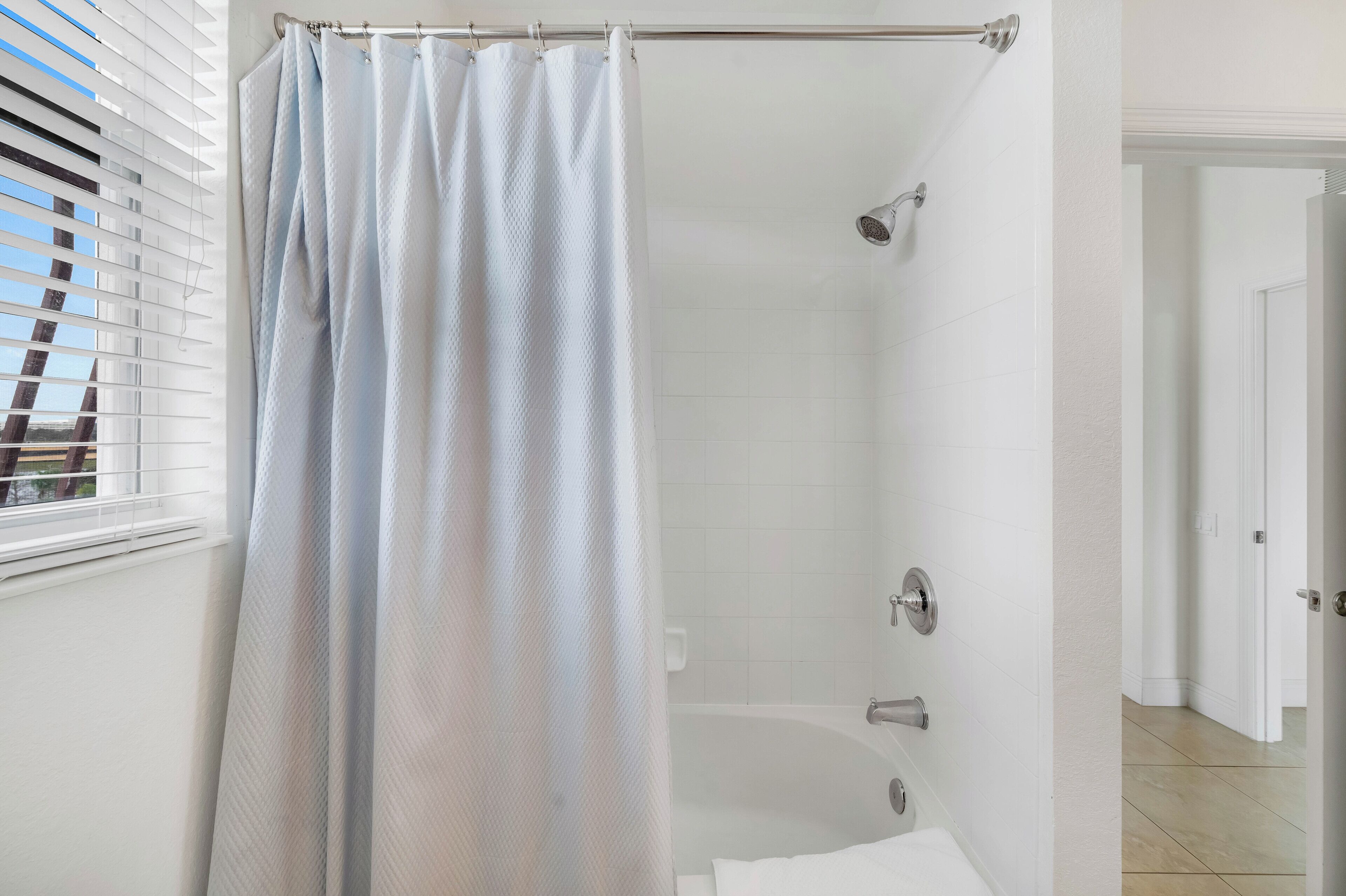 A modern bathroom with a shower, a bathtub, and a window with blinds.