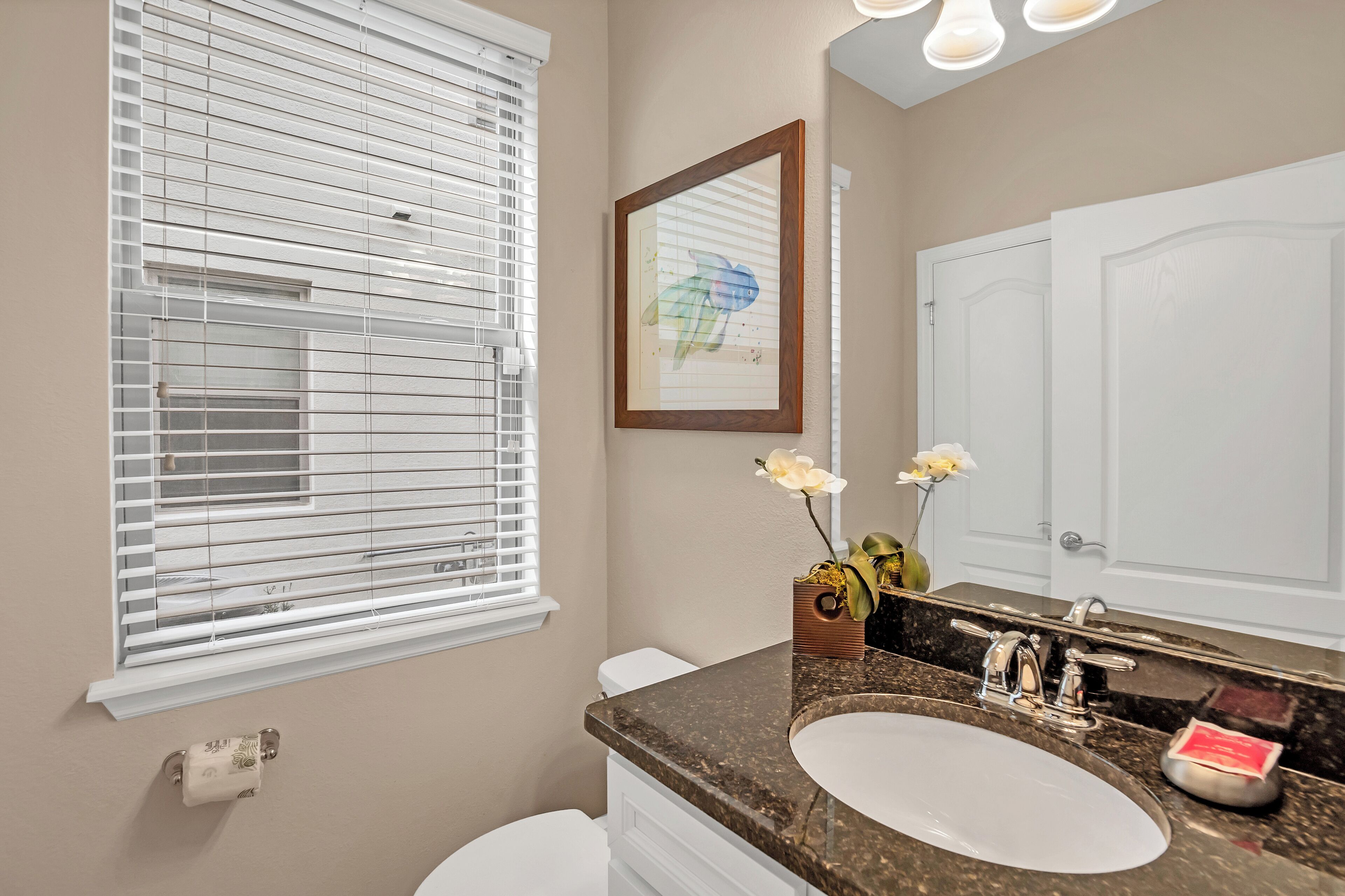 A bathroom with a white toilet, a sink with a marble countertop, and a large mirror.