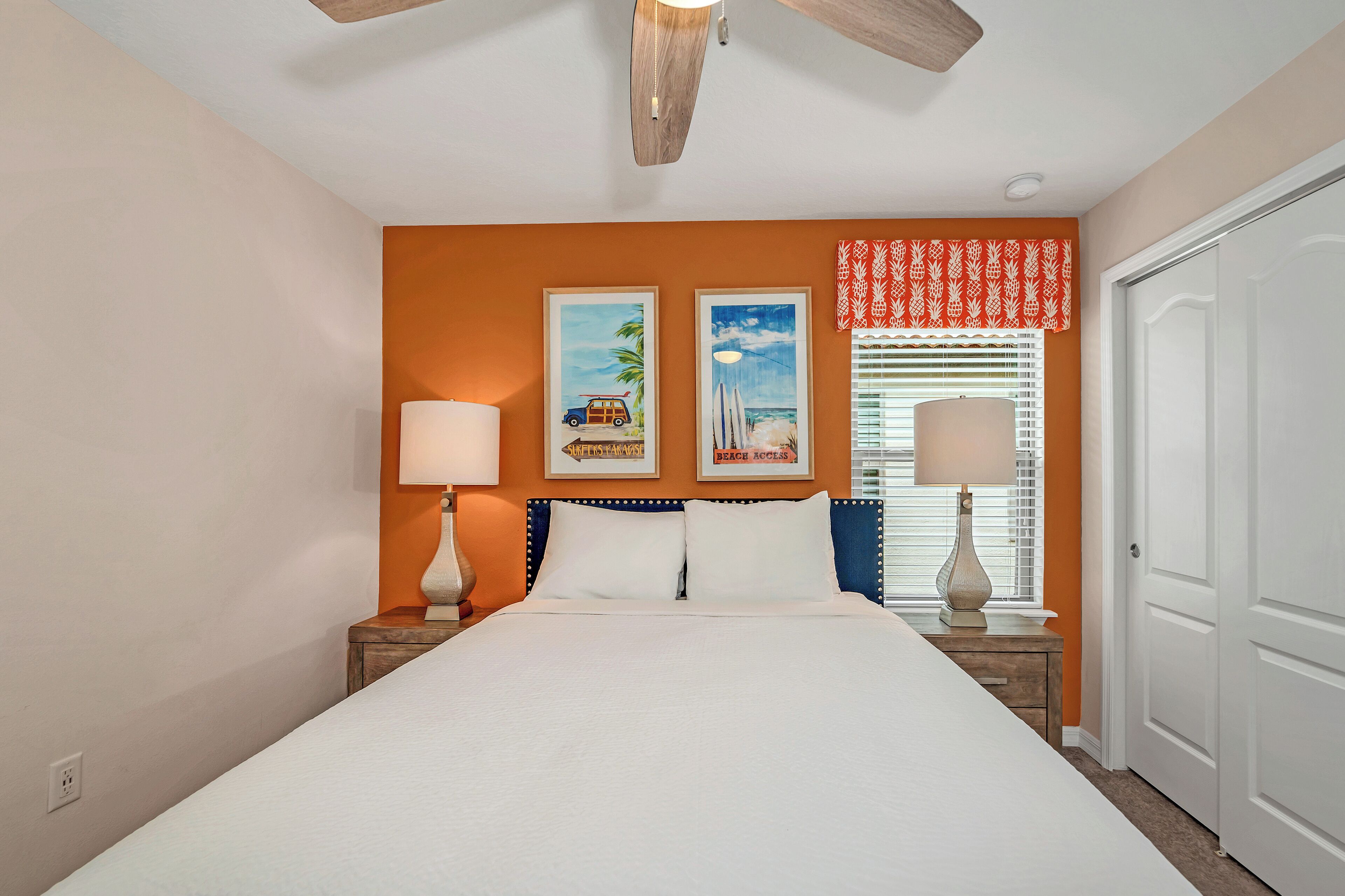 A bedroom with a bed, two bedside lamps, a ceiling fan, and two framed pictures on the wall.