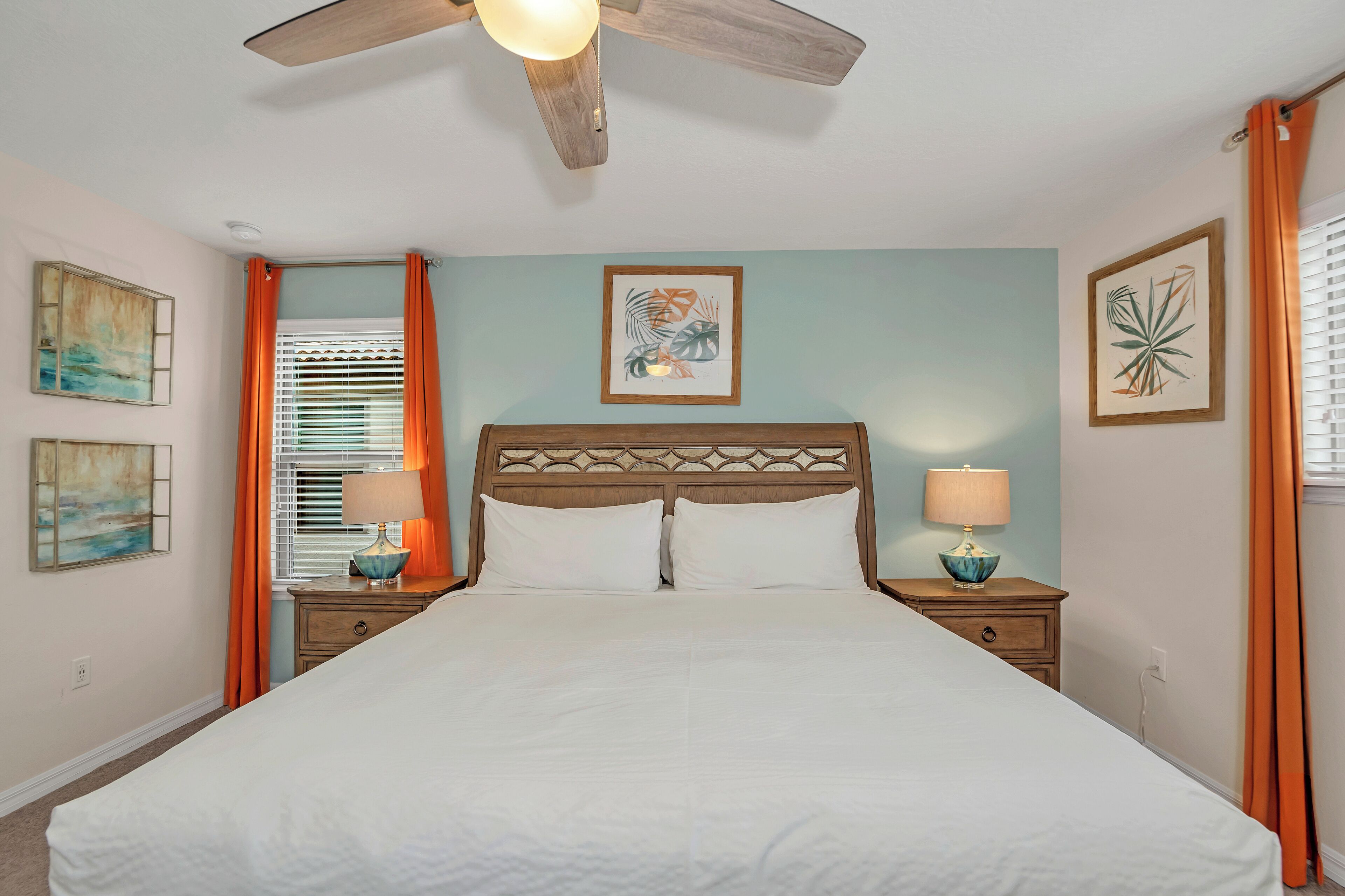A bedroom with a bed, two nightstands, a ceiling fan, and artwork on the walls.