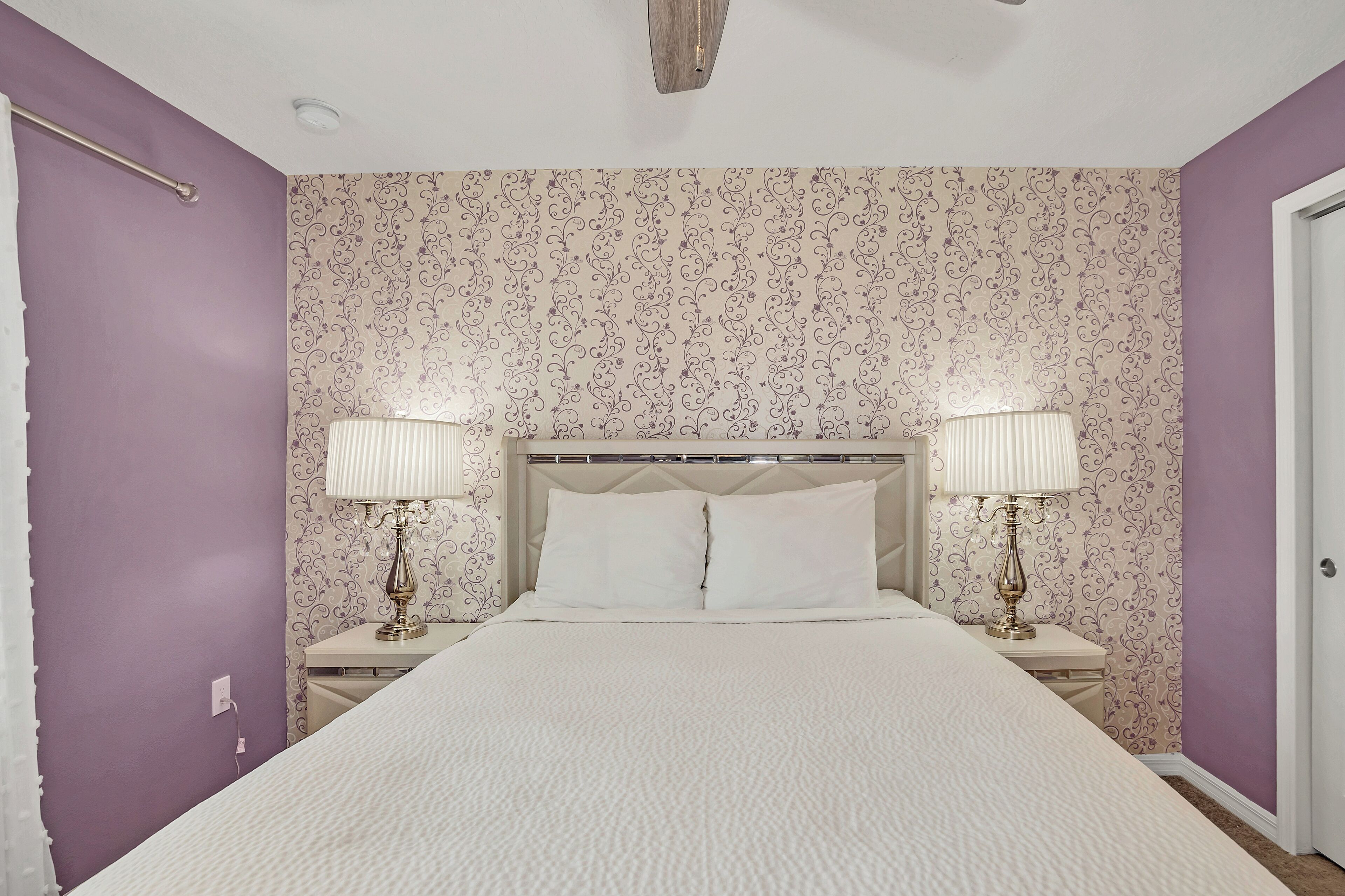 Une chambre à coucher avec un lit, deux tables de chevet avec des lampes, une tête de lit et un papier peint à motifs.