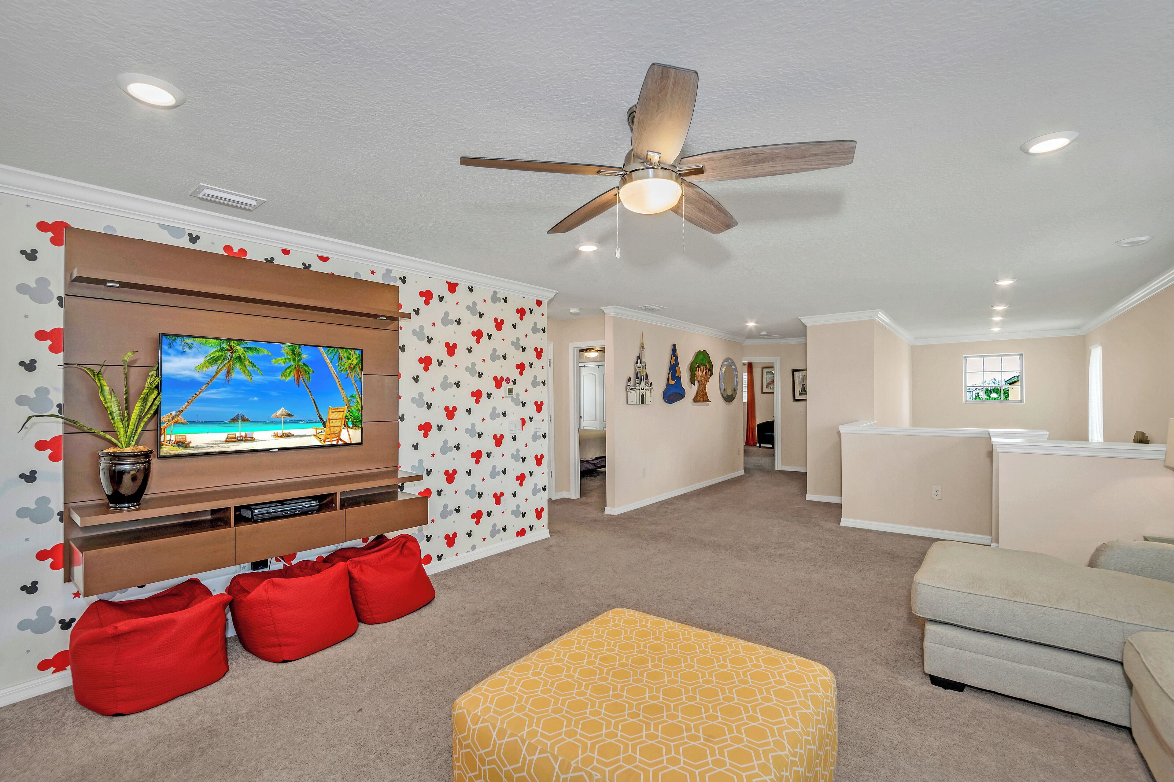 A living room with a TV, ceiling fan, and red bean bags.